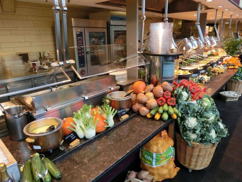 A kitchen servery counter lined with fresh vegetables and prepared dishes